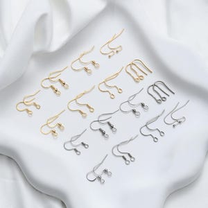 May include: A collection of gold and silver earring hooks. The hooks are arranged in rows on a white surface.