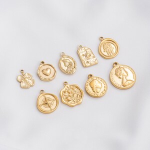 May include: A selection of gold-coloured charms in diverse shapes, including a flower, heart, compass, and coin-like pendants. The charms have a shiny finish, suitable for jewellery making or crafting.