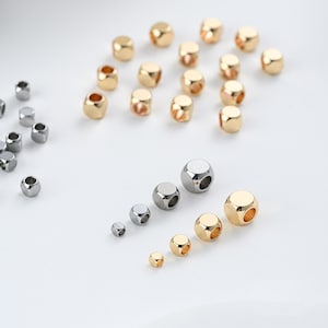 以下が含まれることがあります： 金と銀色の金属ビーズの詰め合わせ。ビーズは立方体型で、角が丸く、穴が開いています。サイズは様々で、他のビーズよりも大きく見えるものもあります。