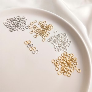 May include: A close-up of three piles of small, oval-shaped jump rings. The jump rings are made of metal and are available in silver, gold, and brass.