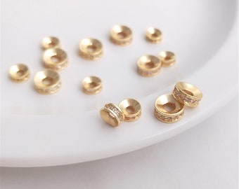 May include: A group of gold-toned metal bead caps with clear rhinestones. The bead caps are arranged on a white surface.