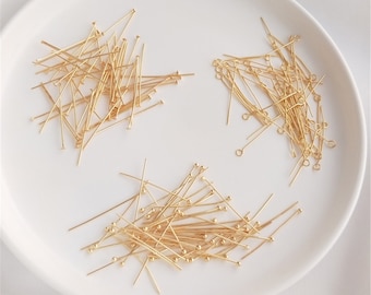 May include: A white plate with three piles of gold-colored head pins. The head pins are arranged in a random pattern. The head pins are used for jewelry making.