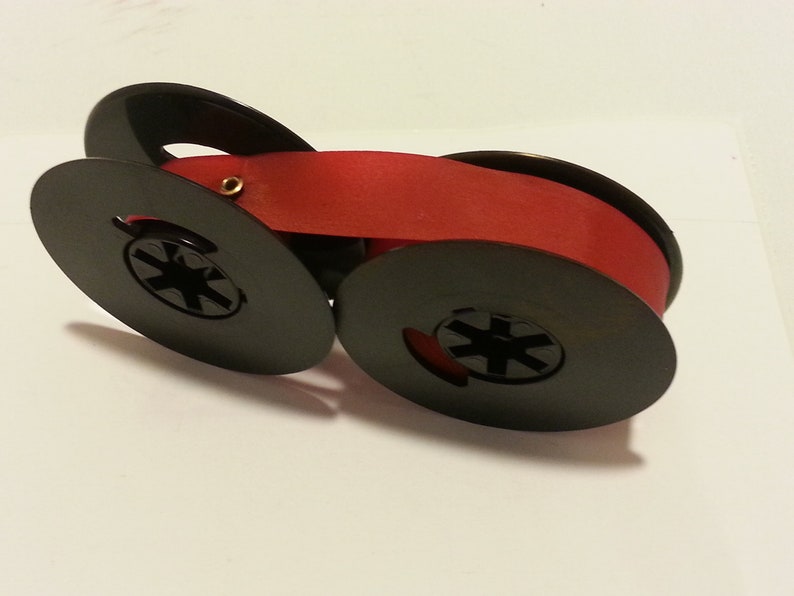 May include: A red typewriter ribbon spool with black plastic spools. The ribbon is wound around the spools.