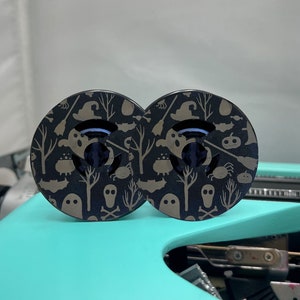 May include: Two black and gold Halloween themed round buttons with a spooky pattern of ghosts, bats, witches, pumpkins, and skulls.