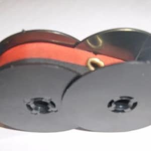 May include: Two black plastic spools with a red ribbon wound around them. The spools have a center hole and a small lip around the edge.