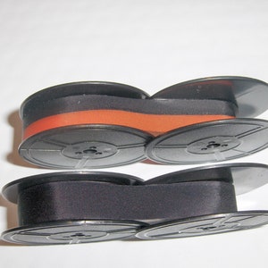 May include: Two black spools of ribbon, one with a black ribbon and one with a black and orange ribbon.