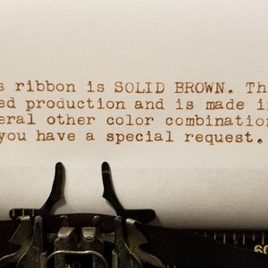 May include: Typewritten text on a white sheet of paper. The text reads: "Hello. This ribbon is SOLID BROWN. This ribbon is in limited production and is made in the USA. We have several other color combinations. Please call us if you have a special request."