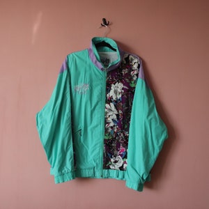 May include: A teal blue windbreaker jacket with a purple and floral print on one side. The jacket has a zip closure and two pockets.