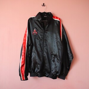 May include: Black satin jacket with red and white stripes on the sleeves. The jacket has a zip fastening and a logo that says "Twin's" on the front.