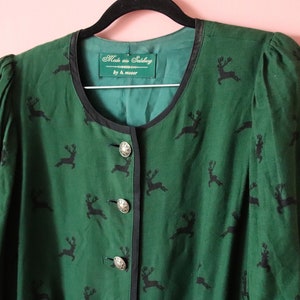 Könnte beinhalten: Eine grüne Jacke mit schwarzem Rentier-Druck und silbernen Knöpfen. Das Etikett lautet "Made aus Salzburg by H. Moser".