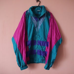 May include: A teal, purple and pink windbreaker jacket with a zip closure. The jacket has a drawstring hood and a contrasting colour design.