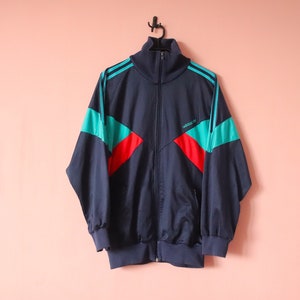 May include: A navy blue Adidas tracksuit jacket with red and turquoise colour blocking and the Adidas logo on the chest.