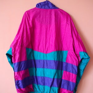 May include: A pink, blue, and teal windbreaker jacket with a zipper closure. The jacket has a striped pattern and a drawstring waist.