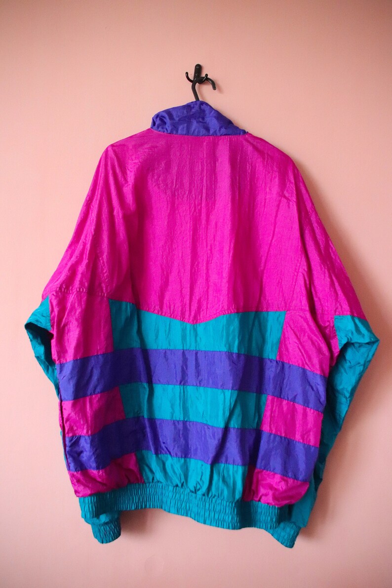 May include: A pink, blue, and teal windbreaker jacket with a zipper closure. The jacket has a striped pattern and a drawstring waist.