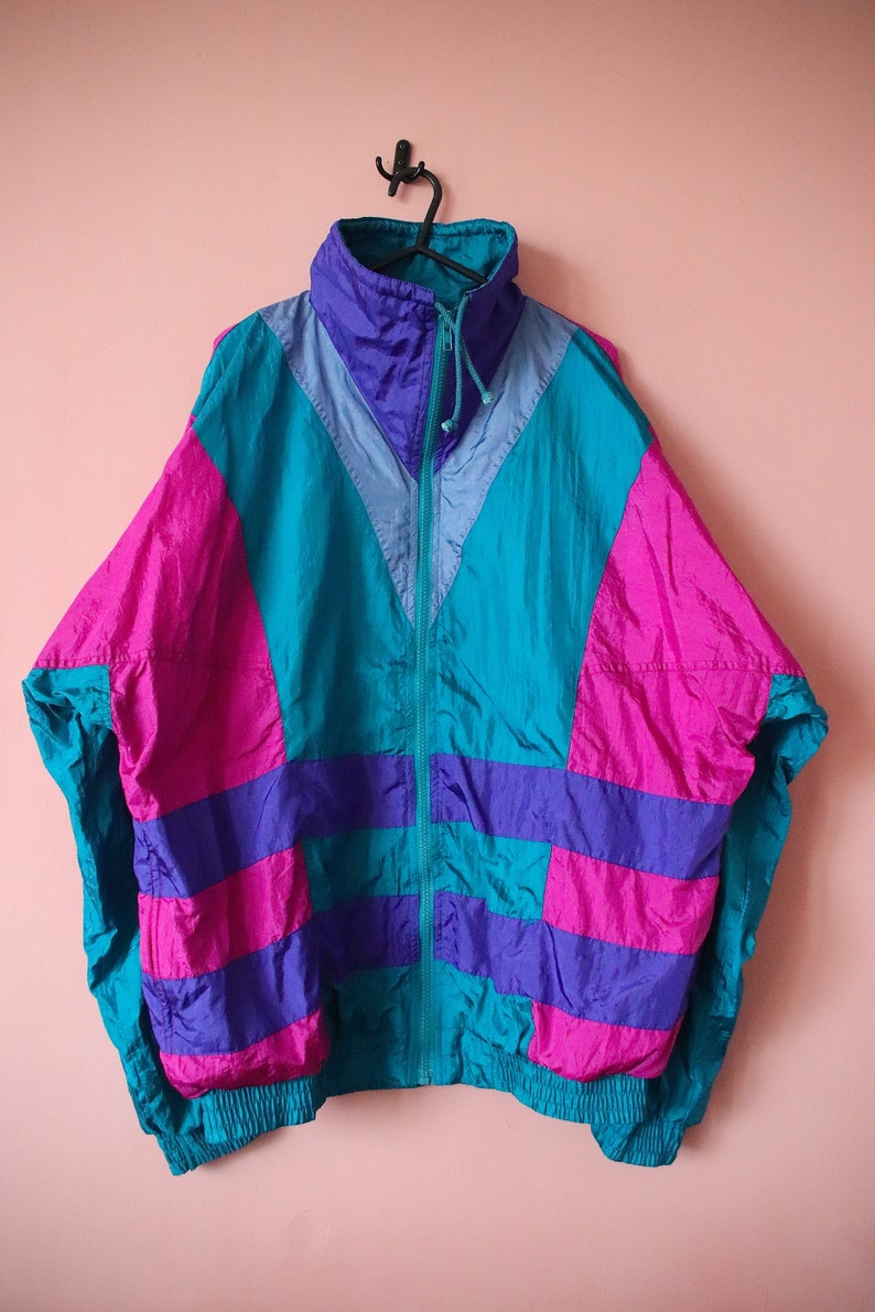 May include: A vintage 90s style jacket with a teal, purple, and pink color block design. The jacket has a zipper closure and a drawstring hood.