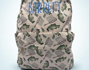 May include: A beige backpack featuring an all-over print of green fish and fishing nets. The name BARRETT is embroidered in blue thread across the upper front section. The bag includes a main compartment and a smaller front zippered pocket.