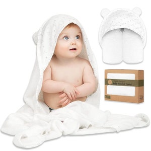 May include: A white baby hooded towel with bear ears, wrapped around a baby. The towel has a subtle pattern. A second towel and a box with the text "Organic Bamboo Baby Hooded Towel" are also shown.
