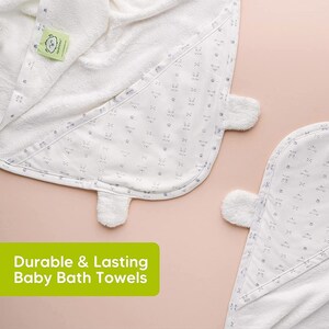May include: White baby bath towels with a hood and a pattern of small gray bunny faces and paw prints. The towels have a soft, plush texture and a tag with a green logo. The text "Durable & Lasting Baby Bath Towels" is displayed in a green rectangle.