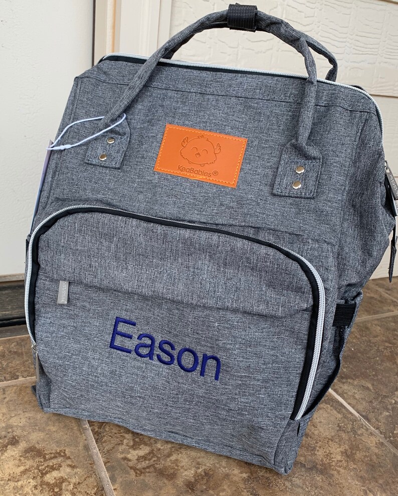 May include: Gray diaper bag backpack with a brown leather patch that says "KeaBabies" and a blue embroidered name "Eason".
