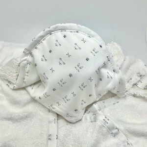 May include: White hooded baby towel with a pattern of gray bunny faces, paw prints, and crossbones. The towel is made of soft, absorbent material, perfect for after bath time. The hood is lined with the same patterned fabric.