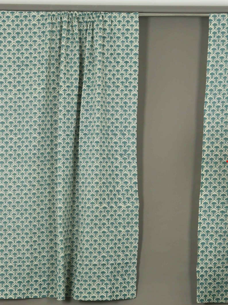 May include: A pair of curtains featuring a repeating teal floral pattern on a cream background. The fabric is gathered at the top along a silver curtain rod, creating vertical folds that drape downward in a consistent, structured arrangement.