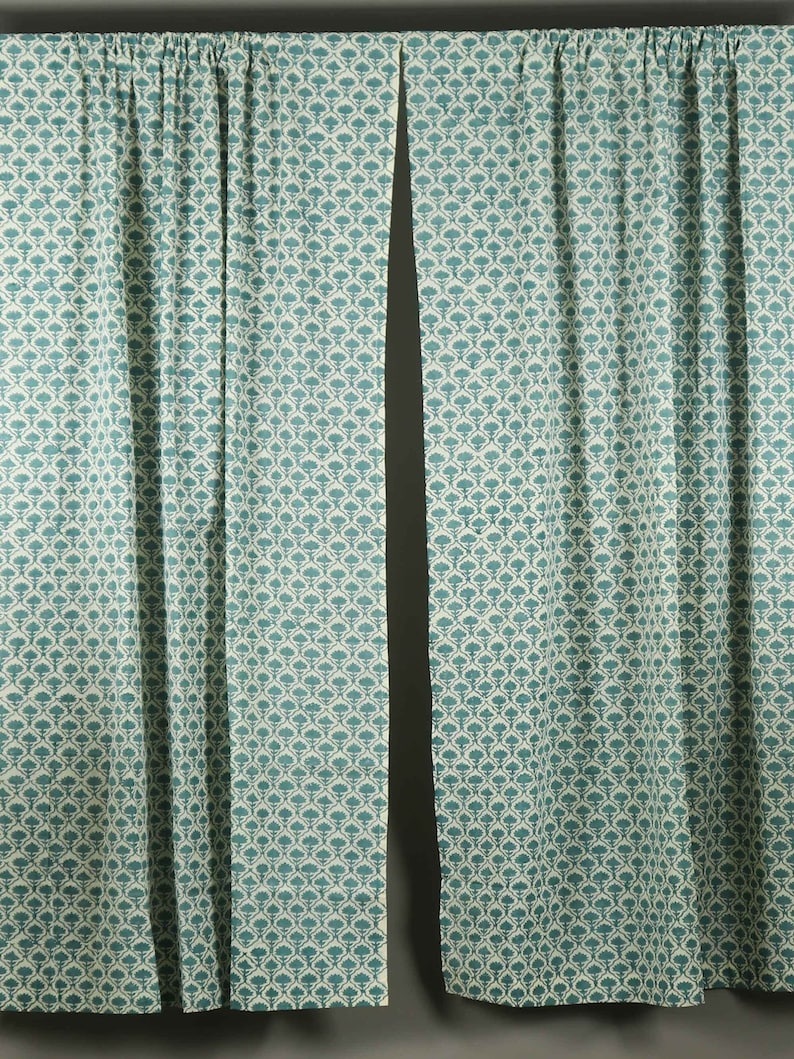 May include: A pair of floor-length curtains featuring a repeating teal and white floral pattern. The fabric is gathered at the top with a rod pocket header, creating vertical folds that extend down the length of the panels to the bottom hem.