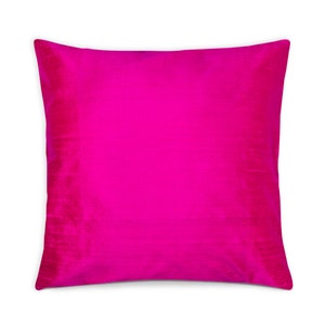May include: A square cushion in a vivid fuchsia hue. The fabric has a smooth, shimmering texture, possibly silk or satin. The solid colour design makes it a versatile accent piece for any room, adding a pop of colour.