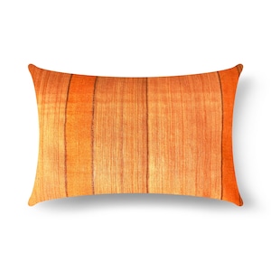 May include: A rectangular throw cushion featuring a vibrant orange fabric with a subtle, textured weave. The surface is decorated with several vertical, thin brown stripes that run across the length of the cushion, creating a simple linear pattern.