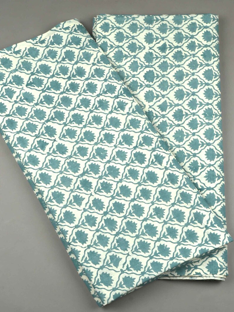 May include: Two folded pieces of fabric featuring a repeating pattern of teal floral motifs set within a white grid. The design consists of stylized flowers centered in each diamond-shaped section, creating a consistent geometric and botanical print.