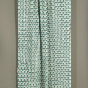 May include: A rectangular curtain panel featuring a repeating teal floral pattern on a cream-colored background. The fabric is gathered at the top along a silver-toned metal rod, creating vertical folds that extend down the length of the textile.