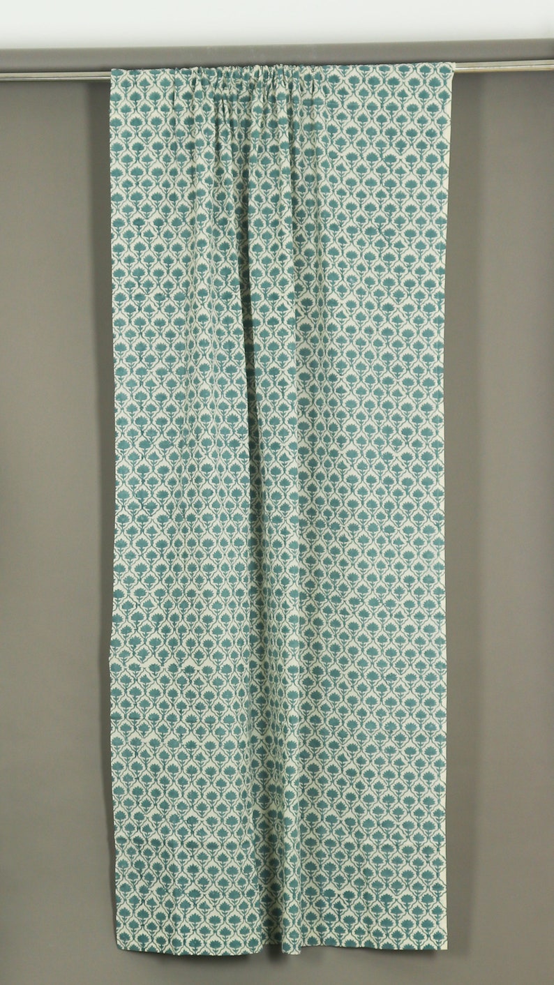 May include: A rectangular curtain panel featuring a repeating teal floral pattern on a cream-colored background. The fabric is gathered at the top along a silver-toned metal rod, creating vertical folds that extend down the length of the textile.