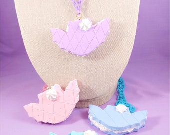 May include: Three pastel-coloured necklaces with a waffle cookie design. The necklaces are made of plastic and have a white frosting detail. The necklaces are displayed on a mannequin.