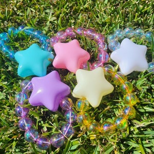 May include: Five colorful star-shaped bracelets with iridescent beads. Each bracelet features a different color star: blue, pink, white, purple, and yellow.