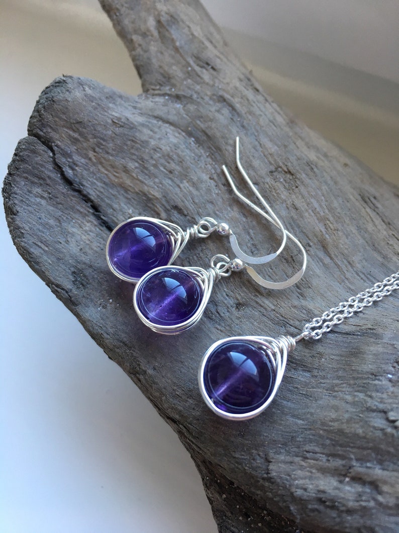 May include: A set of amethyst gemstone earrings and a necklace. The earrings and necklace feature a teardrop-shaped design with a silver wire wrapped around each gemstone.