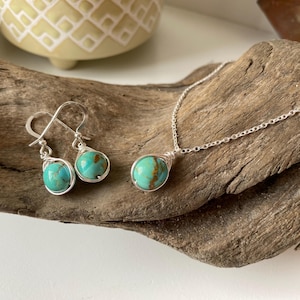 May include: A turquoise stone necklace and earrings set with silver wire wrapping. The stones are a light blue-green color with brown marbling. The necklace has a silver chain.