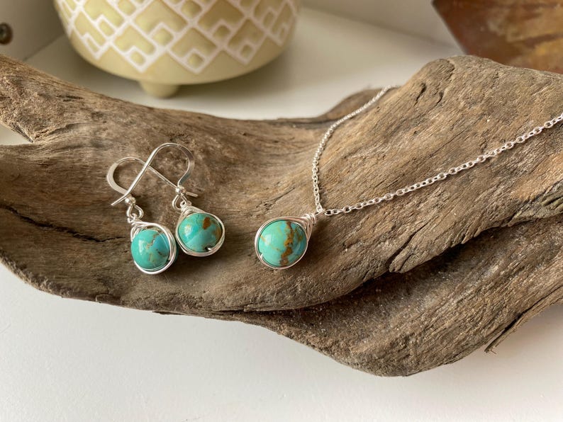 May include: A turquoise stone necklace and earrings set with silver wire wrapping. The stones are a light blue-green color with brown marbling. The necklace has a silver chain.
