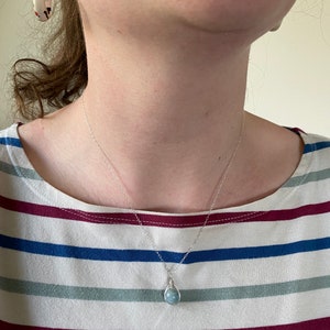 K&ouml;nnte beinhalten: Eine silberne Kettenkette mit einem hellblauen Edelstein-Anh&auml;nger. Der Anh&auml;nger ist mit Silberdraht umwickelt.