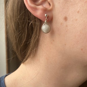 May include: A pair of silver wire wrapped earrings with white moonstone stones.