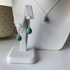 May include: A turquoise gemstone necklace and earrings set with silver wire wrapping. The necklace is on a silver chain and the earrings are dangle style.