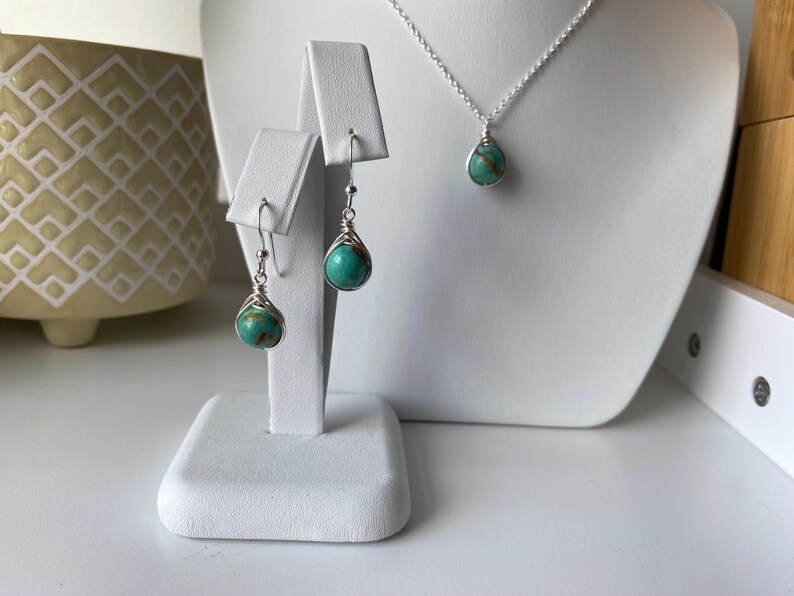 May include: A turquoise gemstone necklace and earrings set with silver wire wrapping. The necklace is on a silver chain and the earrings are dangle style.