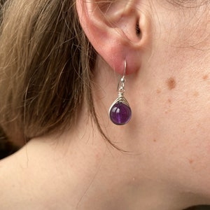 May include: A pair of silver earrings with a purple amethyst gemstone. The earrings are simple and elegant.