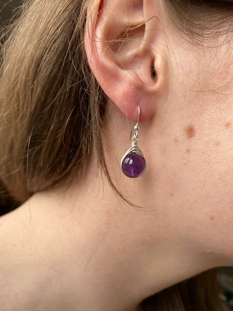 May include: A pair of silver earrings with a purple amethyst gemstone. The earrings are simple and elegant.