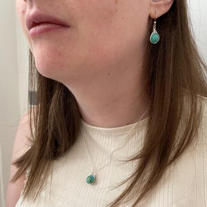 May include: A woman wearing a white top with a silver necklace and earrings featuring turquoise stones.