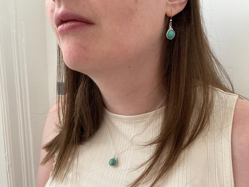 May include: A woman wearing a white top with a silver necklace and earrings featuring turquoise stones.