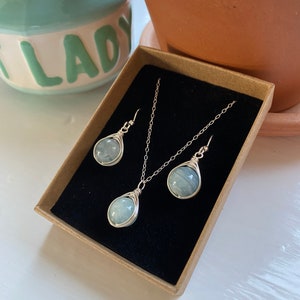 K&ouml;nnte beinhalten: Ein Set aus Aquamarin-Edelsteinschmuck in einer braunen Schachtel. Das Set enth&auml;lt eine Halskette und Ohrringe. Die Steine sind in Silberdraht gewickelt.