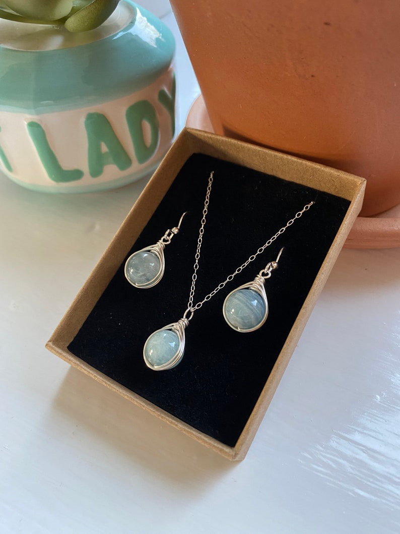 K&ouml;nnte beinhalten: Ein Set aus Aquamarin-Edelsteinschmuck in einer braunen Schachtel. Das Set enth&auml;lt eine Halskette und Ohrringe. Die Steine sind in Silberdraht gewickelt.