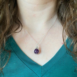May include: A silver chain necklace with a purple gemstone pendant. The pendant is wrapped in silver wire.