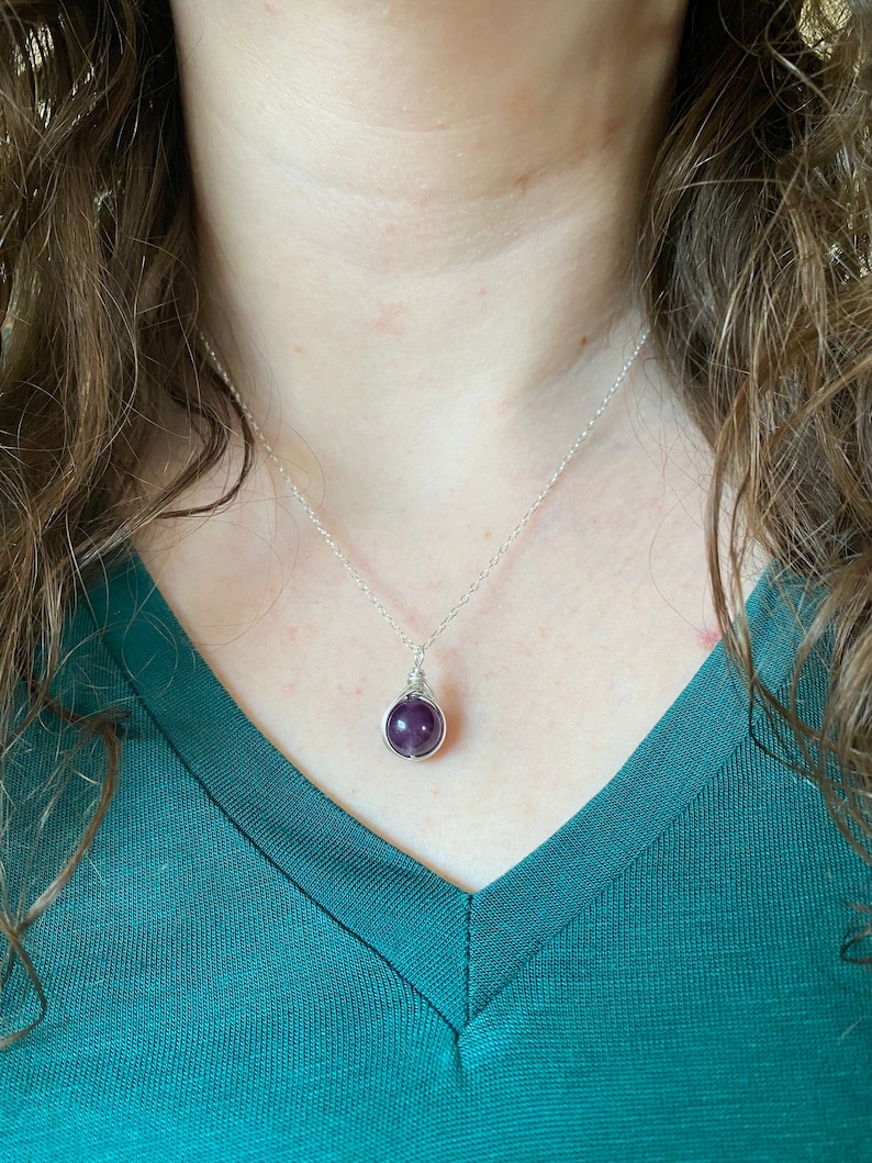 May include: A silver chain necklace with a purple gemstone pendant. The pendant is wrapped in silver wire.