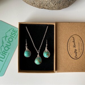 May include: A turquoise gemstone necklace and earrings set in a brown box. The necklace and earrings are made with silver wire and feature a turquoise stone. The box has the text "Crafty Rachael Jewellery" printed on it.
