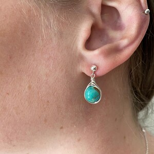 May include: A pair of silver earrings with turquoise stones. The earrings are teardrop shaped and have a wire wrapped design.